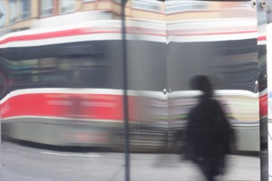 A blurry reflection of a passing streetcar 
                         and a person walking