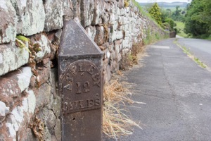 A photo with a very old road marker in the 
                         foreground that reads 'Appleby 12 Miles'