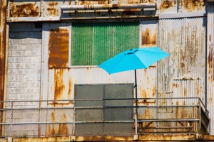 A cheerful, bright, sky-blue umbrella sitting 
                         improbably on a dingy, dirty balcony.